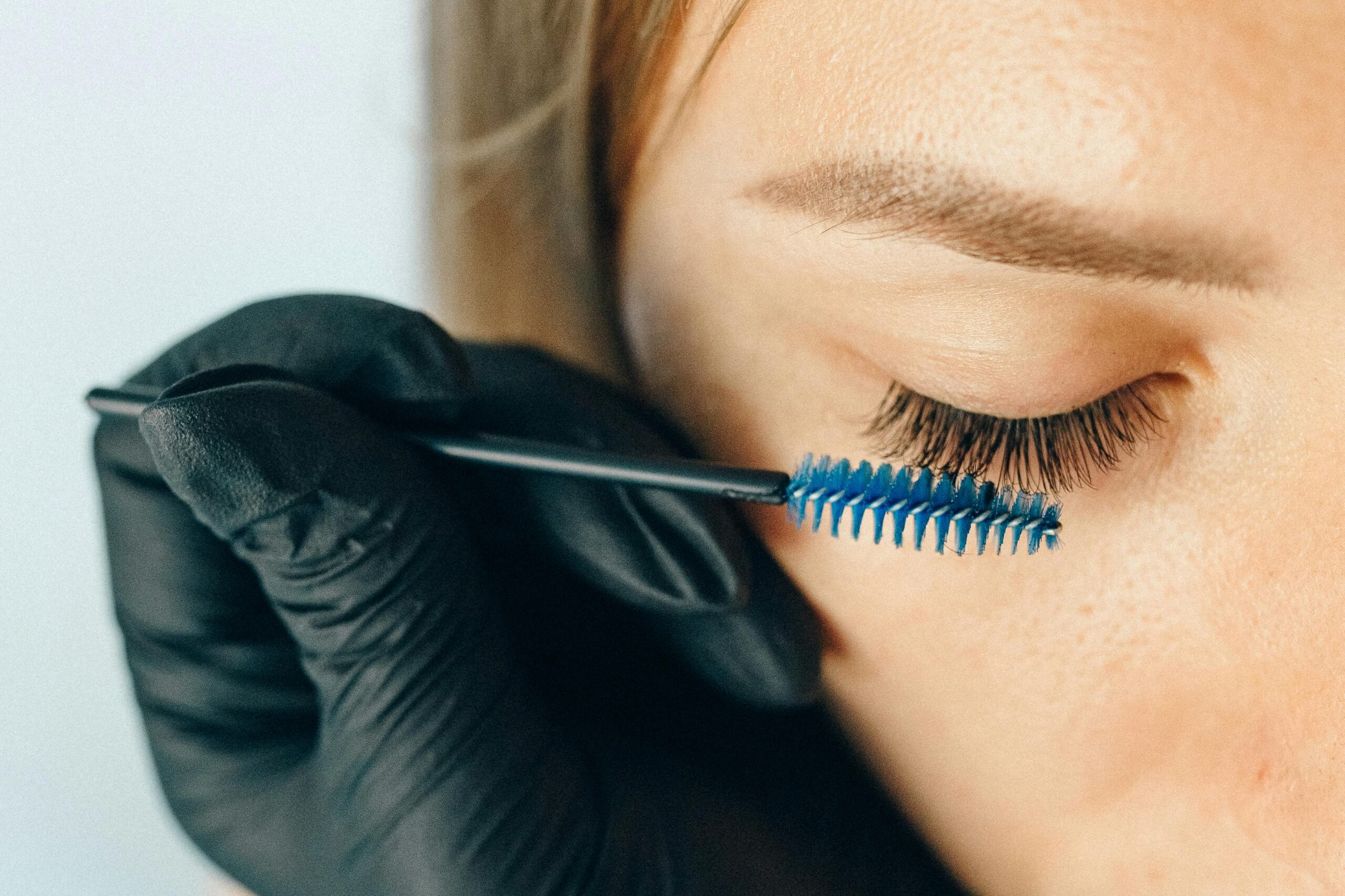 pexels-photo-5128267-5128267 A professional applying eyelash extensions using a blue applicator brush for a refined look.