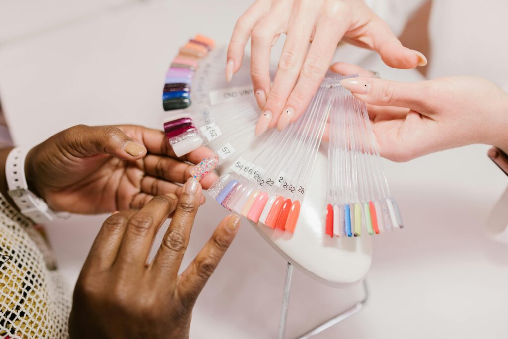 pexels-photo-7755653-7755653 Close-up of hands choosing from a vibrant nail polish sample palette in a salon setting.